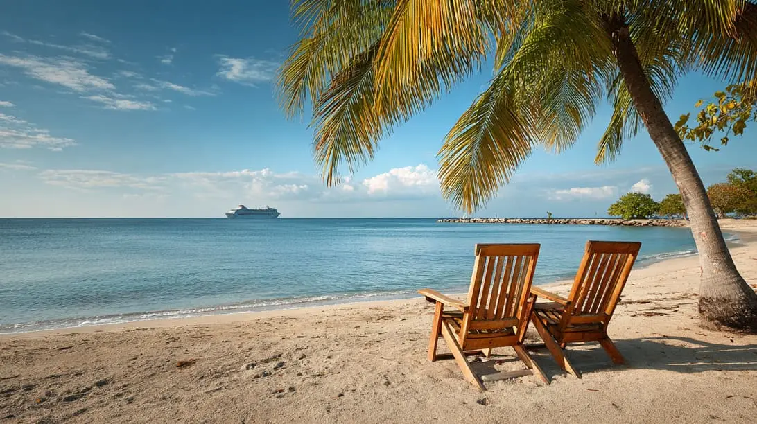 Two wooden lounge chairs sit on a sandy beach under a palm tree, facing the calm sea with a cruise ship visible in the distance.